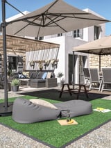 Cour arrière avec bordure grise RUNNEN, gazon artificiel, table de pique-et meubles de patio sous parasol beige.