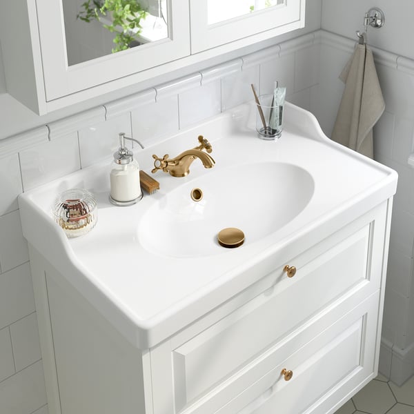 Lavabo de salle de bain blanc avec robinet doré, distributeur de savon et accessoires.