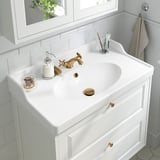 Lavabo de salle de bain blanc avec robinet doré, distributeur de savon et accessoires.