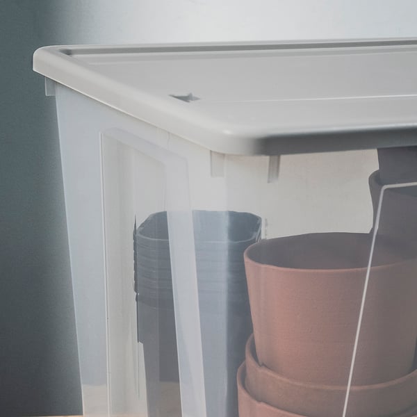 Boîte de rangement blanche avec couvercle gris, partiellement cachée par deux jardinières. Solide, transparent, avec un couvercle sécurisé par une fonction de verrouillage automatique intégrée.