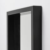 Miroir de sol à cadre noir, réfléchissant la lumière, design moderne et robuste, adapté à la salle de bain ou au salon.