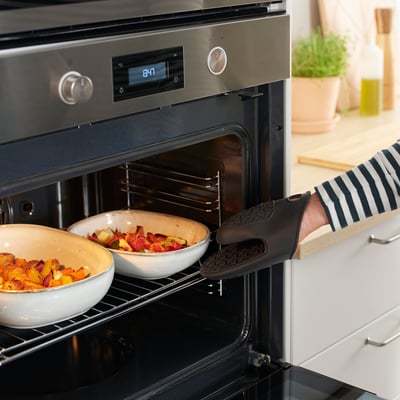 Personne utilisant un gant de cuisine en silicone pour retirer la vaisselle du four. Le gant protège les mains et offre une bonne adhérence.
