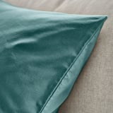 Coussin en velours sarcelle sur tissu beige, texture lisse, détails de coutures apparents.