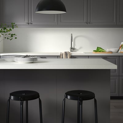 Comptoirs de cuisine modernes avec des tons clairs et foncés contrastés ; tabourets ronds noirs bien positionnés ; Nettoyez les assiettes et les ustensiles sur le comptoir.