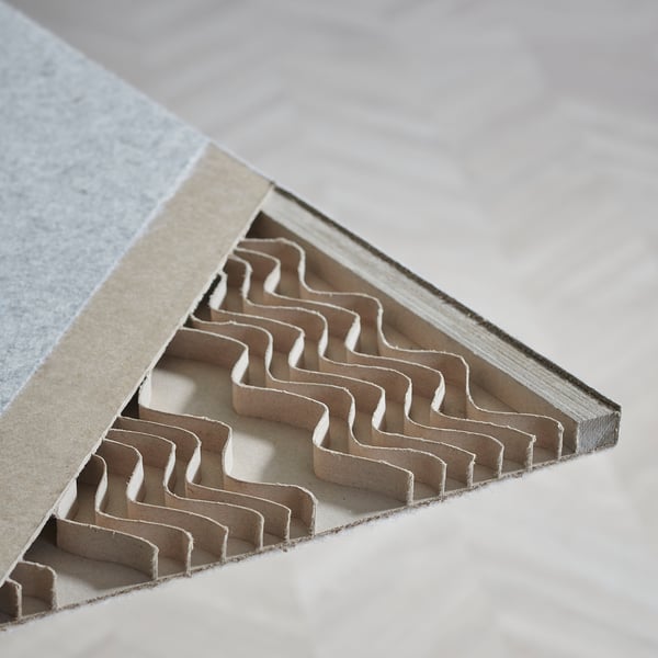Section de séparation de pièce en carton, montrant des fentes complexes et répétitives pour un assemblage facile, placée sur une table. Se concentre sur la qualité du design et l’utilité.
