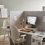 Configuration de bureau moderne avec bureau blanc, chaise grise, moniteur, clavier, souris, lampe et bouteille d’eau. Panneau de séparation de pièce arrière central.