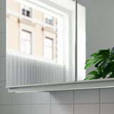 Armoire blanche avec lumière led, bâtiment réfléchissant, plante verte sur carreaux.