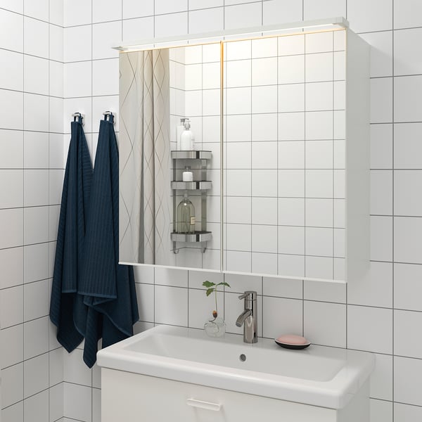 Salle de bain moderne avec carrelage blanc, lavabo, miroir led et serviettes bleu foncé.