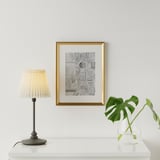 Configuration minimaliste : lampe, cadre doré, plante sur table blanche.