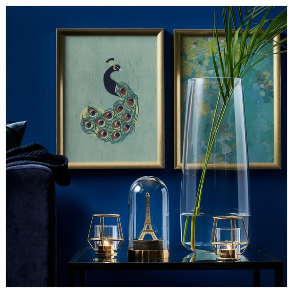 Photo de recette : mur bleu avec art du paon, grand vase, bougies allumées, présentoir de la tour Eiffel, canapé sombre.