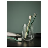 Deux brosses à dents dans un support en verre cannelé transparent sur une surface sombre, mur vert.