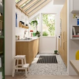 Cuisine moderne avec des armoires en chêne clair SINARP, des comptoirs blancs et un décor minimaliste, avec un petit escabeau blanc.