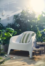 Chaise d’extérieur SKARPÖ blanche moderne, coussin vert rayé, terrasse en bois, verdure luxuriante, lanternes suspendues.