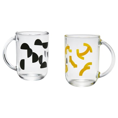 Deux tasses SKEDSTÖR, l’une noire, l’autre jaune, avec des motifs de grains de café et de feuilles, en verre trempé transparent.