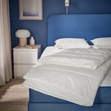 Couette SKOGSFRÄKEN blanche sur lit moderne avec literie bleue.