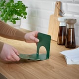 Personne assemblant un porte-serviette en métal vert sur une table en bois, près de la plante et des assaisonnements.