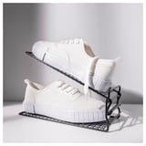 Une paire de baskets blanches repose sur un porte-chaussures en métal noir, ce qui permet de gagner de la place grâce à des étagères réglables.