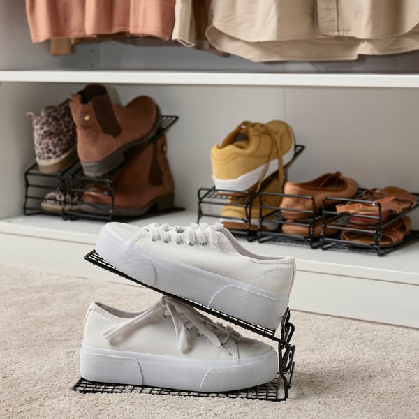 Des baskets blanches sur un porte-chaussures réglable, avec d’autres paires visibles sur des étagères.