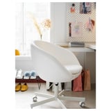 Chaise de bureau blanche moderne avec roues et rembourrage près d’un bureau encombré.