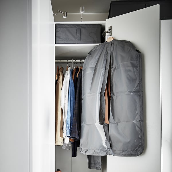 Placard ouvert montrant des vêtements dans des cintres, y compris un sac à vêtements gris et divers vêtements, soigneusement organisés.