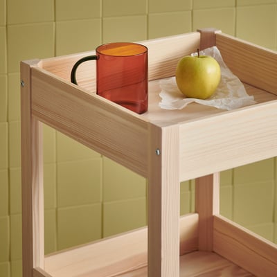 Tasse SKUGGSTUBB & pomme sur plateau en bois clair. Mug ambré contrastant avec le mur vert.