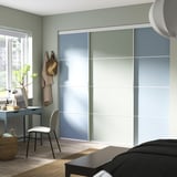 Chambre moderne avec grande armoire coulissante bleu clair. Il s’agit d’un bureau minimaliste, d’une chaise et de plantes décoratives.