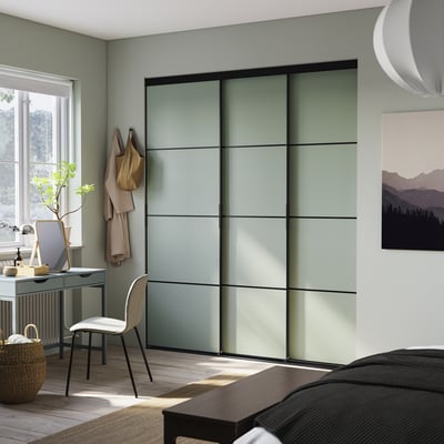 Chambre moderne avec portes de placard coulissantes SKYTTA en verre dépoli vert clair. Configuration minimaliste du bureau et des chaises avec un décor confortable.