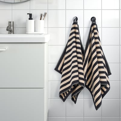 Les serviettes SLÅNHÖSTMAL à rayures noires et beiges sont suspendues à des crochets près de l’évier avec du savon et des brosses à dents.