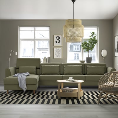 Salon moderne avec grand canapé SLATORP olive, tapis à rayures noires et blanches, suspension en osier et grande fenêtre.