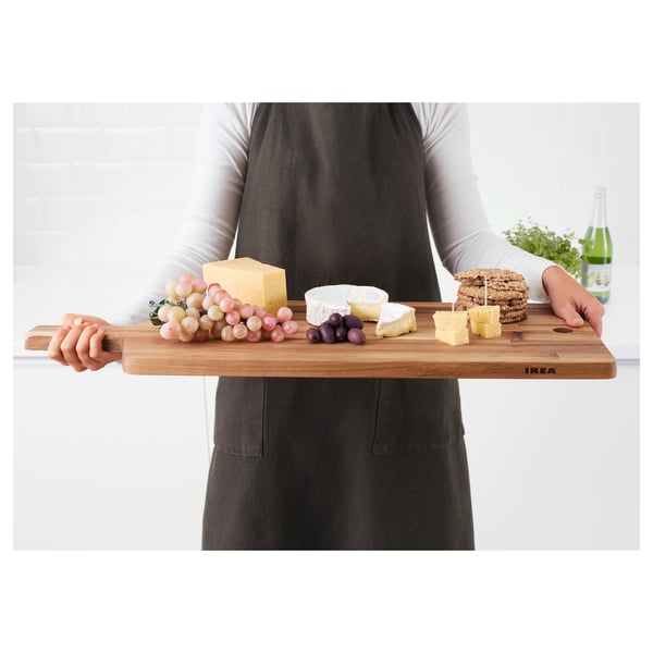 Personne tenant une planche à découper en bois avec du fromage, des raisins et des craquelins, adaptée au service et douce aux couteaux.