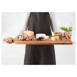 Personne tenant une planche à découper en bois avec du fromage, des raisins et des craquelins, adaptée au service et douce aux couteaux.