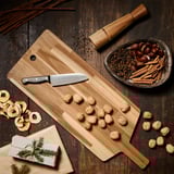 Planche à découper en bois SMÅÄTA avec couteau, noix et bol d’épices et de fruits sur une table.