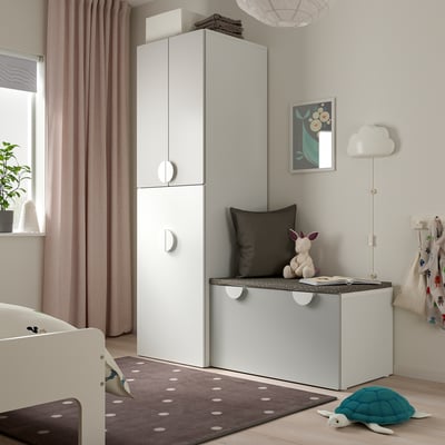 Chambre d’enfant avec armoire SMÅSTAD blanche, coffre à jouets, tapis et berceau. Éclairage tamisé, rideaux et art mural.