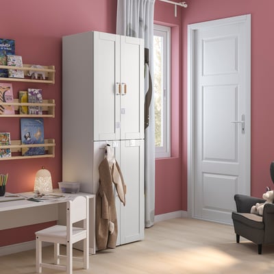 Une armoire SMÅSTAD blanche dans une chambre rose. Il s’accroche pour les vêtements et les tringles. Un petit bureau blanc et une chaise sont devant.