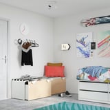 Chambre lumineuse avec art coloré, lit multicolore, banc en bois avec boîtes, oreillers rouges et marron.
