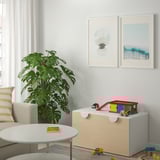 Coffre à jouets SMÅSTAD dans le salon avec jouets et impressions d’art, plante, canapé.