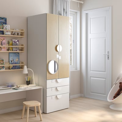 Chambre d’enfant moderne avec armoire SMÅSTAD en bois clair, bureau blanc et étagère remplie de livres colorés. Éclairage tamisé et design minimaliste.