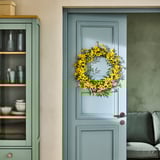 Couronne florale jaune sur la porte bleu pâle, à côté d’une armoire verte avec de la vaisselle.