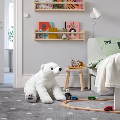 Un grand ours polaire en peluche blanche est assis à côté du lit, entouré d’un petit train et de livres sur des étagères.
