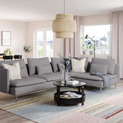 Salon moderne avec un grand canapé sectionnel SÖDERHAMN gris, une suspension élégante, un tapis coloré et de grandes fenêtres offrant une vue sur la ville.
