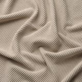 Tissu beige doux, en velours côtelé, avec des lignes ondulées et parallèles, drapé en douceur, mettant en valeur texture et confort.