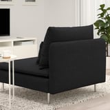 Canapé moderne noir avec assise profonde et pieds en métal, positionné dans un salon confortable. Une table d’appoint avec une tasse à café se trouve à côté.