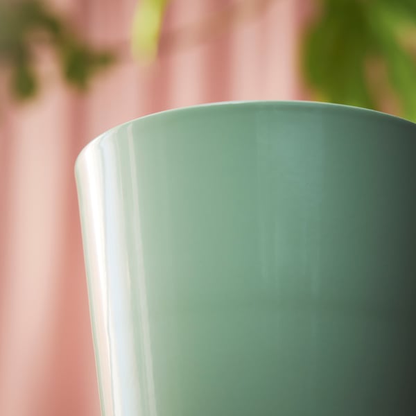 Gros plan d’un pot vert lisse et brillant, montrant une texture de qualité, sur un fond rose doux.