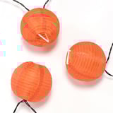 Trois lanternes orange brillantes sont suspendues dans une rangée décorative, reliées par des fils noirs, projetant une lumière chaude et ambiante.