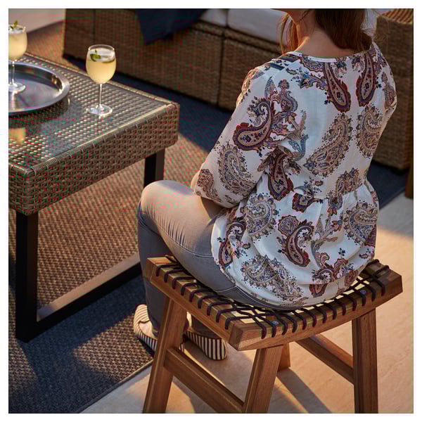Personne sur le tabouret STACKHOLMEN, chemise à motifs, boisson à proximité.