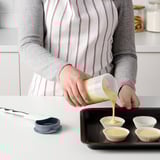 Personne versant du liquide d’un shaker gradué dans des moules à muffins.