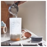 Verser la poudre à la main dans une tasse à mesurer transparente avec couvercle noir.