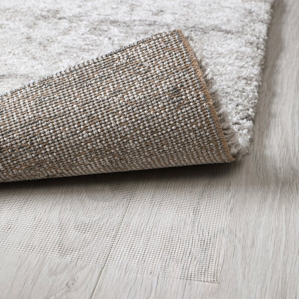 Un tapis gris enroulé avec des poils épais et texturés, posé sur un parquet en bois clair. Le tissage dense suggère le confort et l’absorption acoustique.