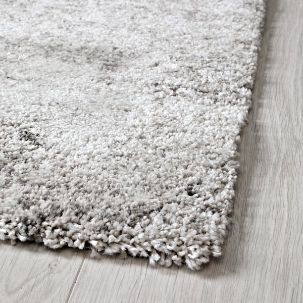 Coin de tapis gris moelleux sur le parquet, texture douce visible.