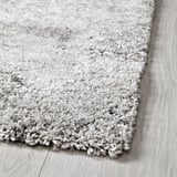 Coin de tapis gris moelleux sur le parquet, texture douce visible.